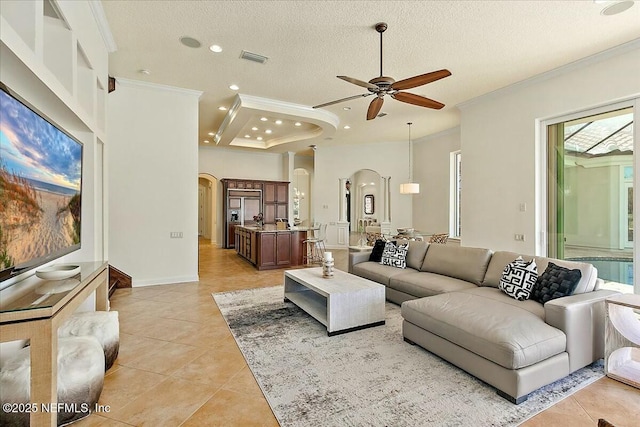 living area with light tile patterned floors, arched walkways, a ceiling fan, and crown molding