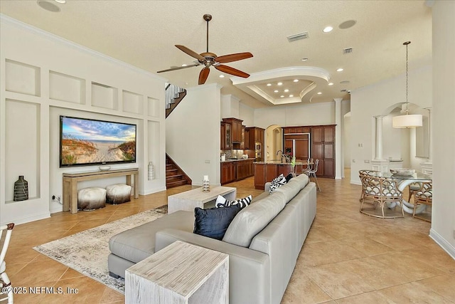 living area with arched walkways, visible vents, crown molding, and ceiling fan