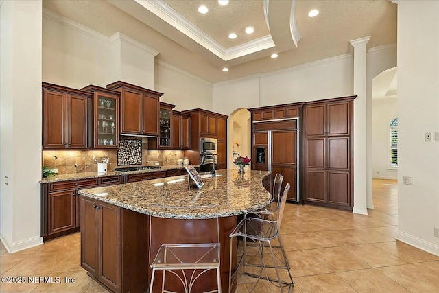 kitchen with a kitchen bar, arched walkways, built in appliances, and ornamental molding