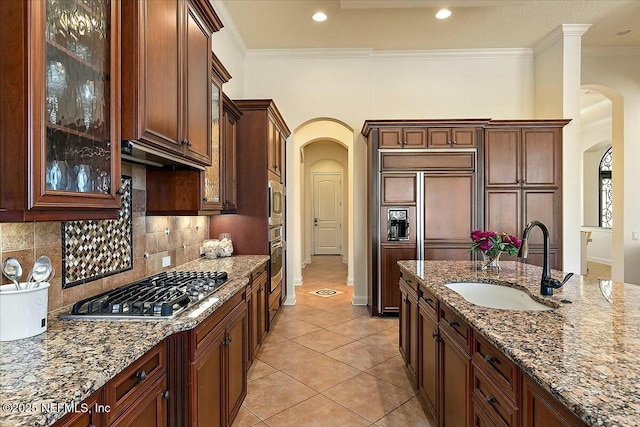 kitchen with crown molding, light stone countertops, arched walkways, stainless steel appliances, and a sink