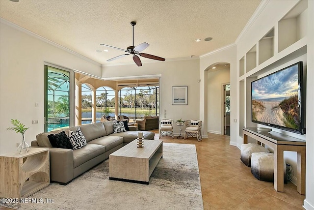 living room with crown molding, ceiling fan, light tile patterned floors, arched walkways, and a textured ceiling