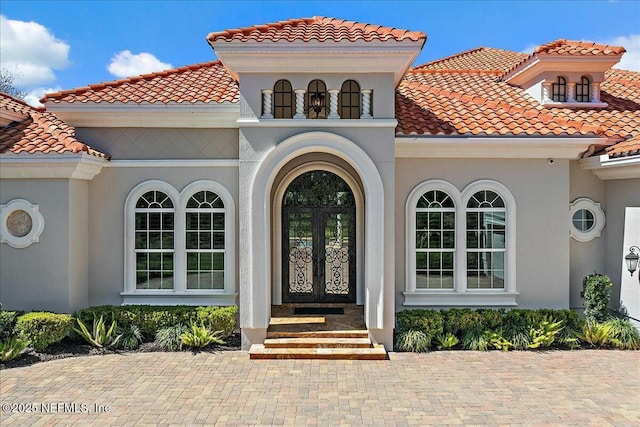 view of exterior entry with french doors, stucco siding, and a tile roof