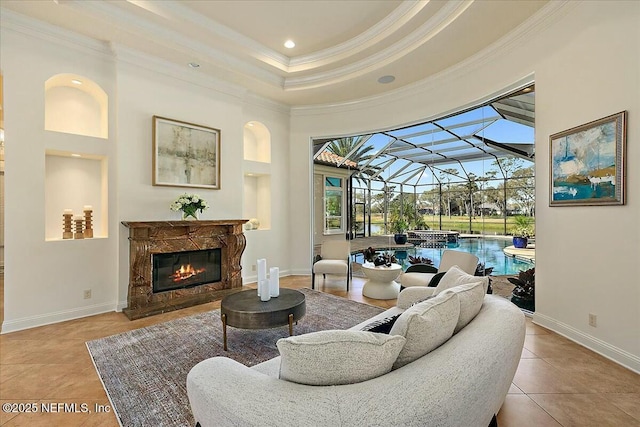 tiled living area featuring baseboards, a tray ceiling, a high end fireplace, a sunroom, and ornamental molding