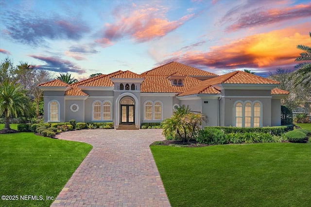 mediterranean / spanish-style home featuring decorative driveway, french doors, a yard, and stucco siding