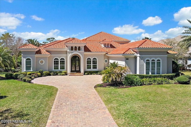 mediterranean / spanish home with a front yard, decorative driveway, a tile roof, and stucco siding