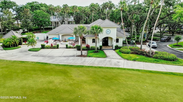 view of front facade with stucco siding, driveway, a tile roof, and a front yard