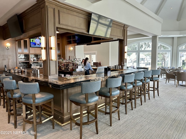 bar featuring indoor wet bar, beam ceiling, light colored carpet, and a towering ceiling