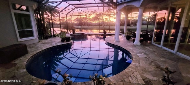 pool at dusk with glass enclosure, a pool with connected hot tub, and a patio