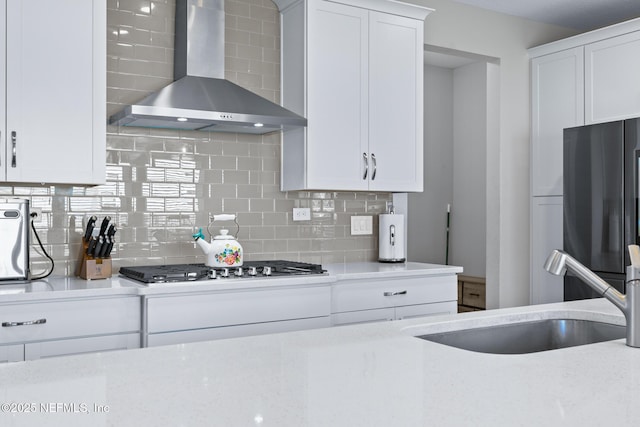 kitchen with a sink, white cabinetry, stainless steel appliances, wall chimney range hood, and decorative backsplash
