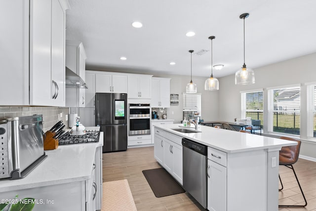 kitchen with backsplash, a sink, stainless steel appliances, wall chimney range hood, and visible vents