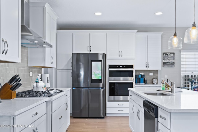 kitchen featuring a sink, hanging light fixtures, stainless steel appliances, wall chimney range hood, and white cabinets