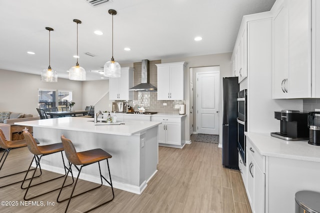 kitchen with a breakfast bar area, backsplash, a sink, wall chimney range hood, and white cabinets