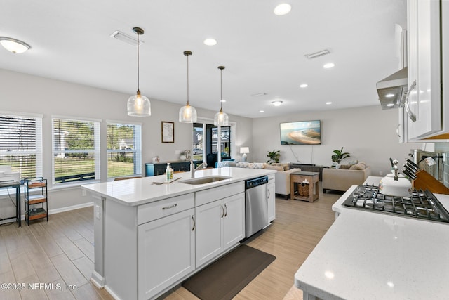 kitchen with appliances with stainless steel finishes, white cabinetry, a sink, open floor plan, and wall chimney range hood