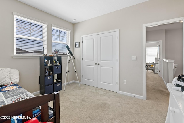 bedroom with light colored carpet, a closet, multiple windows, and baseboards