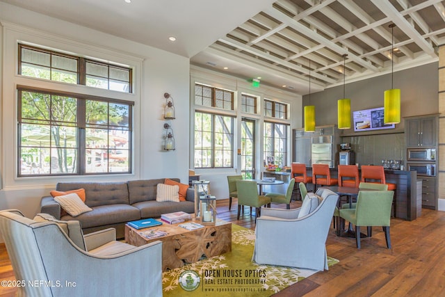 living area featuring wood-type flooring, a high ceiling, recessed lighting, and a healthy amount of sunlight