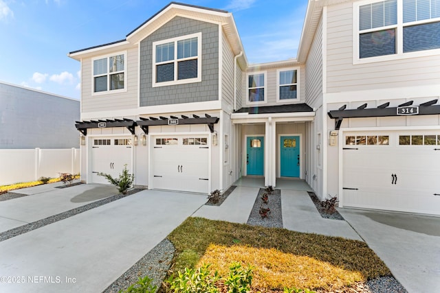 view of property featuring an attached garage, concrete driveway, board and batten siding, and fence