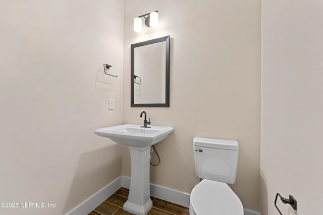 bathroom featuring toilet, wood finished floors, baseboards, and a sink