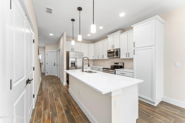 kitchen with wood finish floors, a sink, tasteful backsplash, stainless steel appliances, and white cabinets