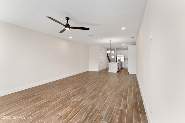 unfurnished living room featuring recessed lighting, ceiling fan with notable chandelier, baseboards, and wood finished floors