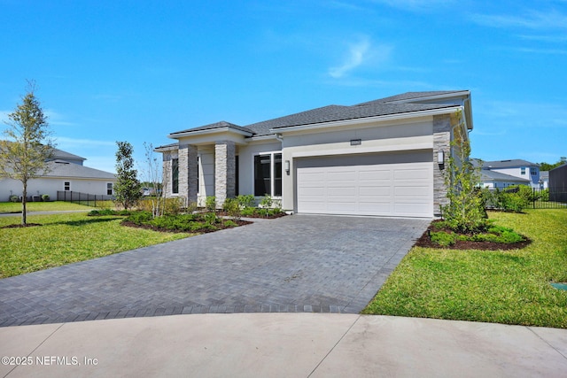 prairie-style house with a front yard, fence, an attached garage, stone siding, and decorative driveway