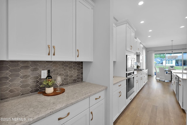 kitchen featuring light wood-style flooring, white cabinets, appliances with stainless steel finishes, pendant lighting, and backsplash