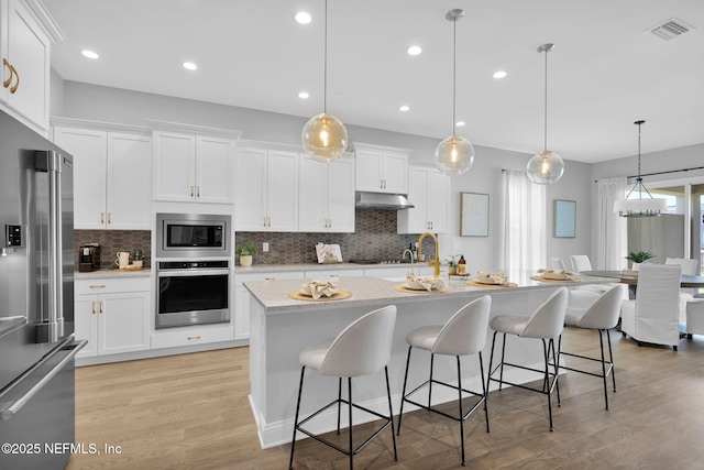 kitchen featuring under cabinet range hood, visible vents, appliances with stainless steel finishes, and white cabinetry