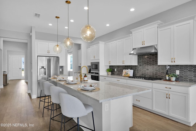 kitchen featuring visible vents, under cabinet range hood, stainless steel appliances, light wood finished floors, and decorative backsplash