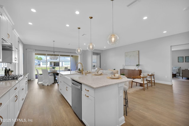 kitchen featuring visible vents, light wood-style flooring, stainless steel appliances, a sink, and a kitchen bar