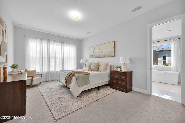 carpeted bedroom featuring ensuite bath, baseboards, and visible vents