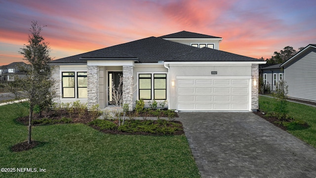 view of front of house with an attached garage, a yard, stucco siding, stone siding, and decorative driveway