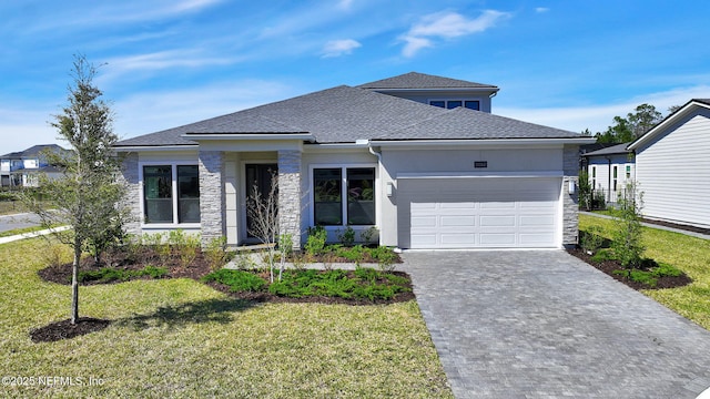 prairie-style home featuring an attached garage, a shingled roof, a front lawn, stone siding, and driveway