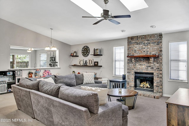 carpeted living room with plenty of natural light, vaulted ceiling with skylight, a brick fireplace, and a ceiling fan