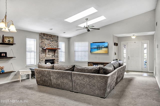 carpeted living room featuring a chandelier, vaulted ceiling with skylight, a brick fireplace, and baseboards