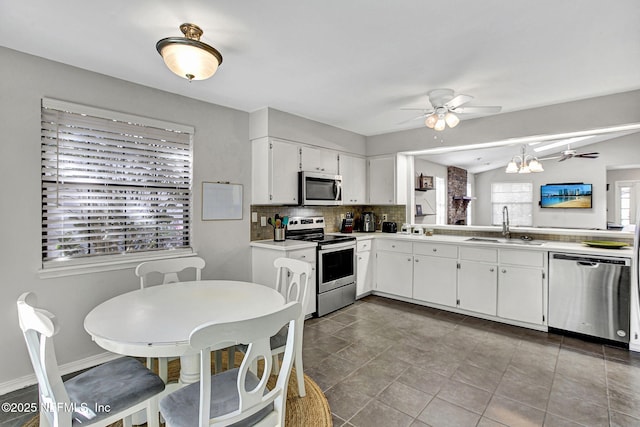 kitchen with light countertops, ceiling fan with notable chandelier, appliances with stainless steel finishes, white cabinetry, and a sink