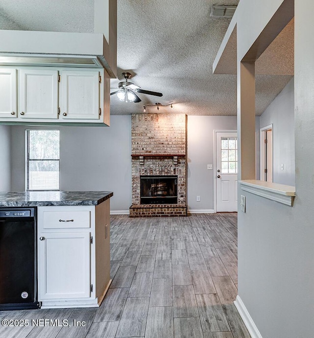 kitchen with wood finish floors, ceiling fan, a fireplace, white cabinets, and a textured ceiling