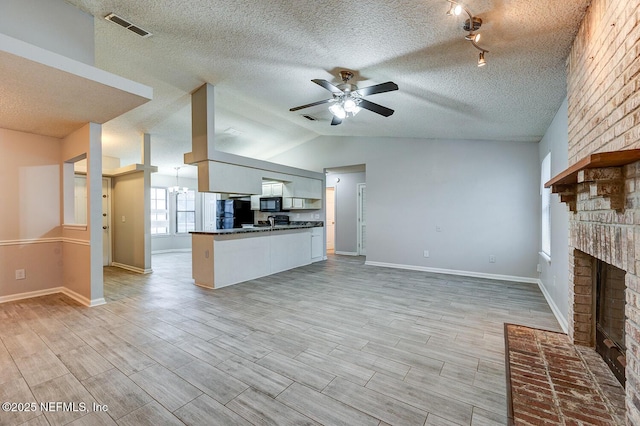 unfurnished living room featuring a brick fireplace, ceiling fan with notable chandelier, visible vents, and wood finish floors