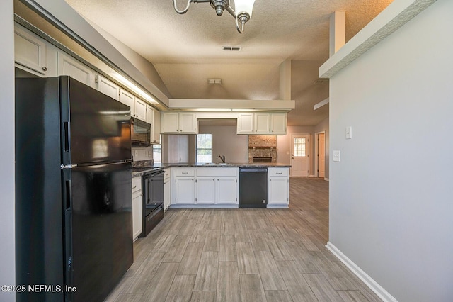 kitchen featuring visible vents, wood tiled floor, black appliances, vaulted ceiling, and dark countertops