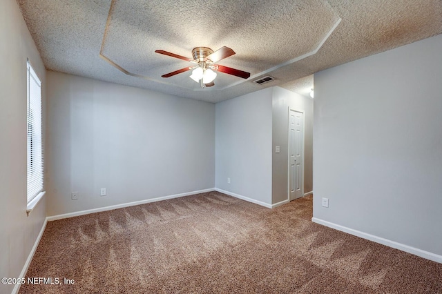 carpeted empty room with visible vents, a textured ceiling, baseboards, and ceiling fan