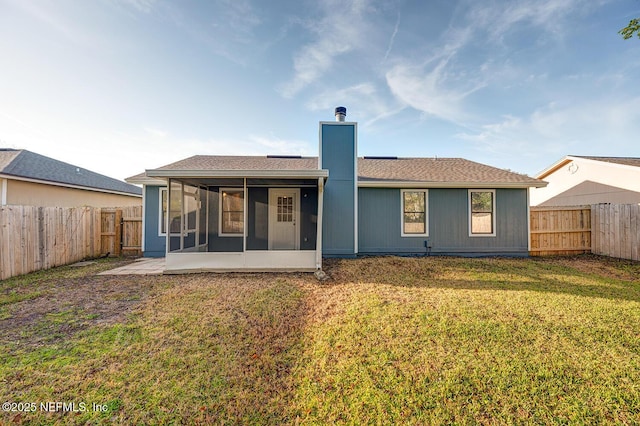 rear view of property featuring a yard, a fenced backyard, a chimney, and a sunroom