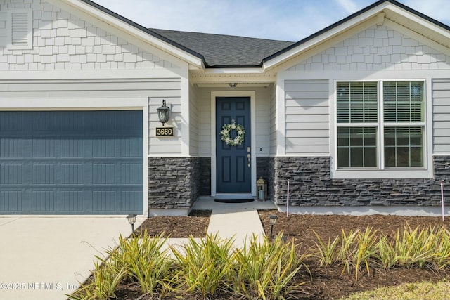 view of exterior entry featuring a garage, stone siding, roof with shingles, and driveway