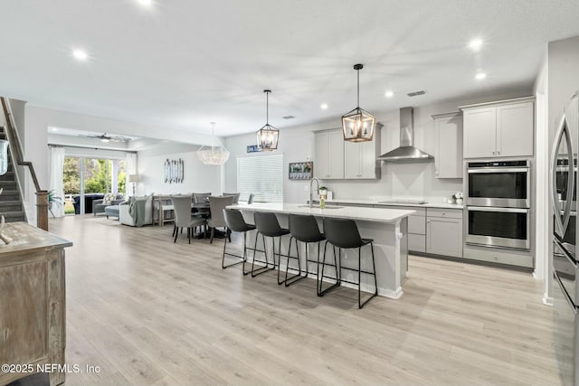 kitchen featuring a kitchen breakfast bar, open floor plan, stainless steel appliances, light wood-style floors, and wall chimney range hood