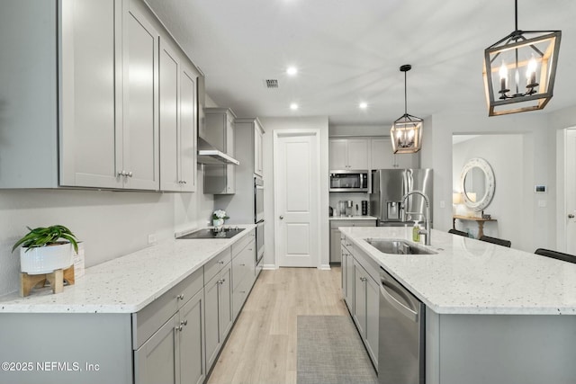 kitchen featuring a chandelier, gray cabinets, appliances with stainless steel finishes, light wood-style flooring, and a sink