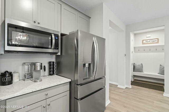 kitchen featuring baseboards, light stone countertops, gray cabinets, appliances with stainless steel finishes, and light wood-style floors