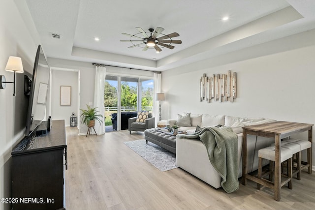 living area with visible vents, recessed lighting, ceiling fan, a raised ceiling, and light wood-type flooring