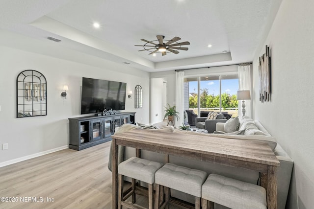 dining room with visible vents, a ceiling fan, baseboards, light wood finished floors, and a raised ceiling