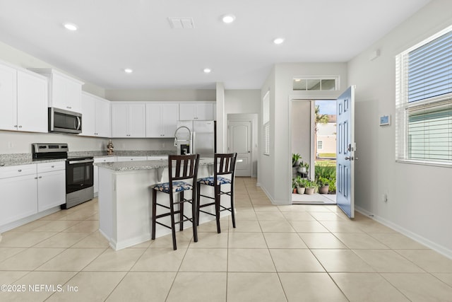 kitchen featuring an island with sink, recessed lighting, light tile patterned flooring, appliances with stainless steel finishes, and white cabinetry