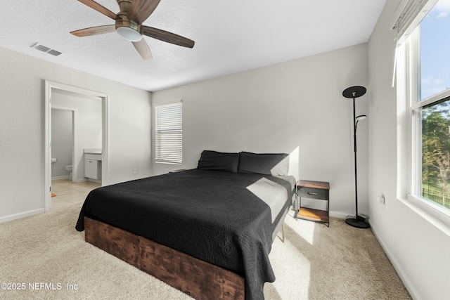 bedroom featuring visible vents, baseboards, ceiling fan, light colored carpet, and ensuite bathroom