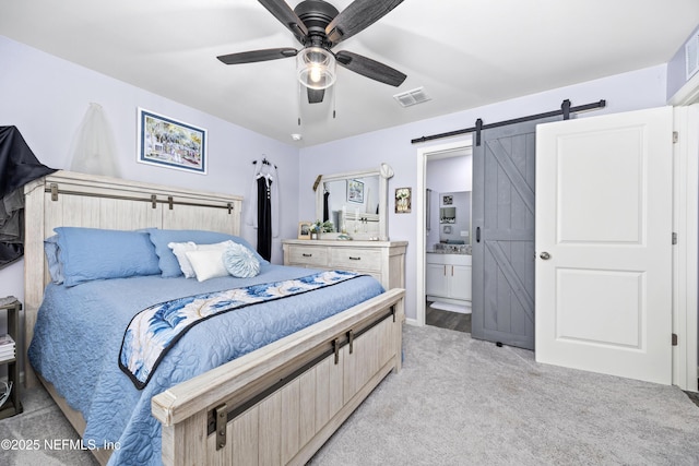 bedroom with visible vents, ensuite bathroom, a barn door, light colored carpet, and ceiling fan