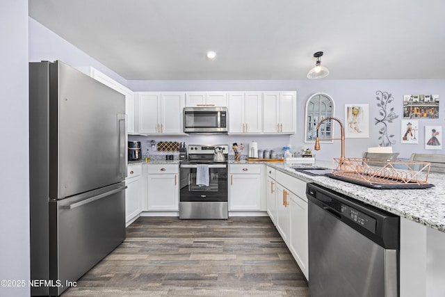 kitchen with a sink, light stone counters, stainless steel appliances, white cabinets, and dark wood-style flooring