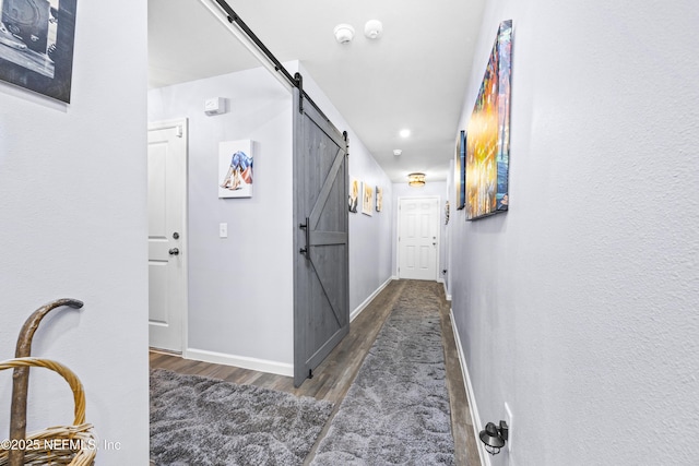 hallway featuring a barn door, baseboards, and wood finished floors